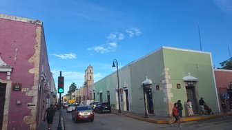 Bunte Gebäude in Valladolid, Mexiko, mit einem grünen und rosa Farbton, unter einem klaren blauen Himmel.