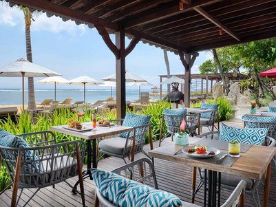 Ein einladendes Restaurant am Strand mit stilvollen Tischen und Stühlen, umgeben von Palmen und Sonnenschirmen.