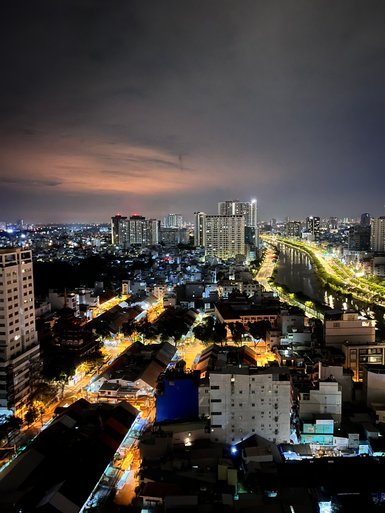 Ein nächtlicher Blick auf die beleuchteten Straßen von Saigon, mit Hochhäusern und einem ruhigen Fluss im Hintergrund.