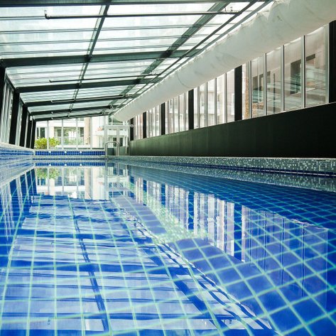 Ein moderner Innenpool mit klarem, blauem Wasser, umgeben von großen Fenstern, die viel Tageslicht hereinlassen.