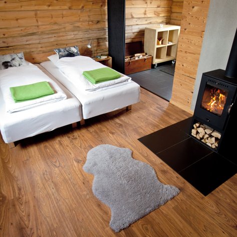 Ein gemütliches Zimmer mit zwei Einzelbetten, grünen Decken und einem modernen Kamin, der einladend flackert.