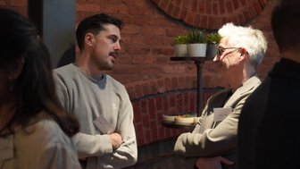 Zwei Männer unterhalten sich angeregt in einem modernen Raum mit Backsteinwänden und Pflanzen auf einem Tisch.