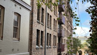 Eine schmale Gasse mit Backsteingebäuden, in der Bäume sanft über die Ziegelmauern hängen.