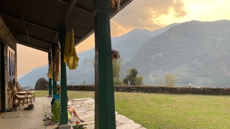 Zwei Personen sitzen entspannt auf einer Veranda und genießen den Blick auf die Berge bei Sonnenuntergang.