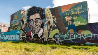 Ein großes Wandgemälde zeigt ein Porträt eines lächelnden Mannes mit Brille, umgeben von bunten Pflanzenmotiven.