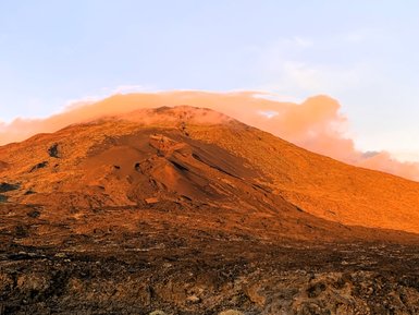 Der majestätische Vulkan Teide erhebt sich über die karge, lavaartige Landschaft, beleuchtet von warmem Sonnenlicht.