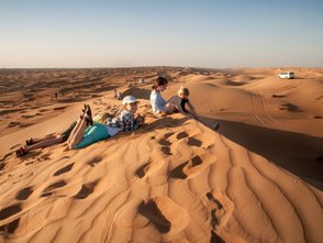 Kinder sitzen gemeinsam auf einer Wüstendüne – Oman Familienreise