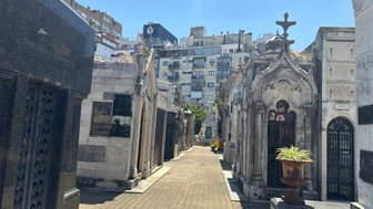 Ein sonniger Tag im Friedhof von Buenos Aires, mit eleganten Grabstätten und modernen Gebäuden im Hintergrund.
