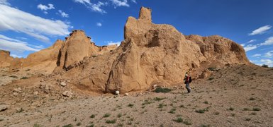 Ein Wanderer erkundet die beeindruckenden, sandfarbenen Felsformationen unter einem strahlend blauen Himmel in der Mongolei.