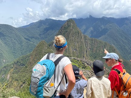 Eine Gruppe von Menschen steht auf einem Aussichtspunkt und bewundert die Ruinen von Machu Picchu inmitten der Berge.
