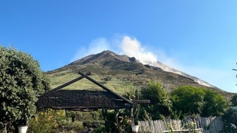 Der Blick auf den Stromboli zeigt einen rauchenden Vulkan unter einem strahlend blauen Himmel, umgeben von üppiger Vegetation.