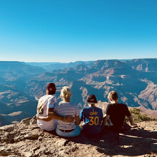 Eine Gruppe von vier Personen sitzt am Rand des Grand Canyon und genießt die atemberaubende Aussicht auf die Landschaft.