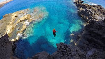 Ein Abenteurer springt von einer Klippe in das glitzernde, türkisfarbene Wasser vor der Küste Madeiras.