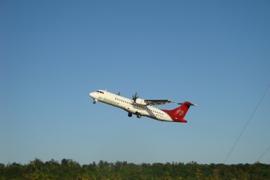Ein Flugzeug von Air Madagascar hebt in den blauen Himmel ab, während die grüne Landschaft im Hintergrund sichtbar ist.