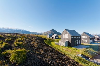 Eine malerische Landschaft mit modernen, schwarzen Ferienhäusern vor einem majestätischen Berg und klarem Himmel.
