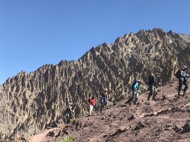 Eine Gruppe von Wanderern erklimmt einen steilen, felsigen Pfad in einer beeindruckenden Berglandschaft unter klarem Himmel.