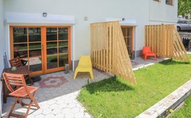 Ein sonniger Außenbereich mit Holzstühlen und bunten Sitzgelegenheiten, umgeben von grünem Gras und einem gepflegten Garten.