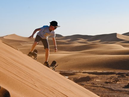 Kind gleitet mit einem Sandboard die sandigen Dünen der Wüste hinunter – Familienreise nach Marokko