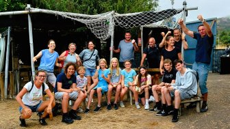 Eine fröhliche Gruppe von Menschen posiert vor einer rustikalen Kulisse, alle strahlen Freude und Zusammenhalt aus.