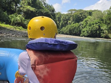 Eine Person in einem roten und blauen Schwimmwesten sitzt in einem Schlauchboot auf einem ruhigen Gewässer.