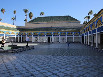Ein weitläufiger Innenhof mit einem Brunnen, umgeben von bunten Gebäuden und Palmen unter einem klaren blauen Himmel.