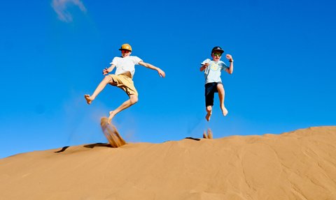 Kinder genießen die Freiheit und springen voller Freude auf den weiten Sanddünen der Wüste – Marokko Reise mit Kindern
