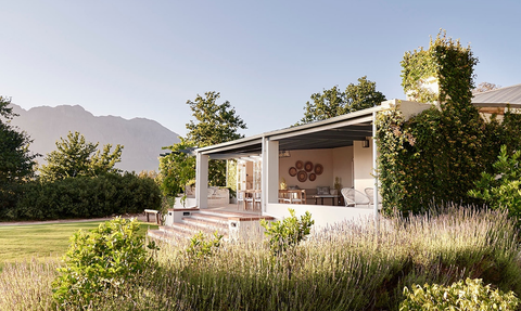 Ein charmantes Cottage umgeben von üppigem Grün und Lavendel, mit Blick auf majestätische Berge im Hintergrund.