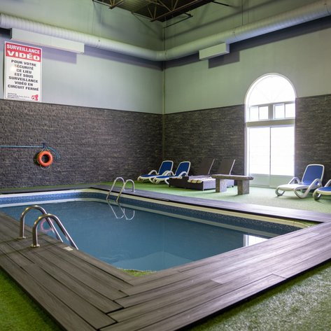 Ein Innenpool mit blauen Liegen und einem Holzsteg, umgeben von grünem Teppich und einer Steinwand.
