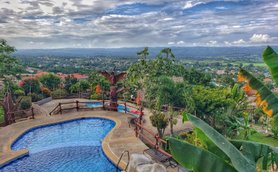 Ein atemberaubender Blick auf einen Pool, umgeben von üppigem Grün und einer malerischen Landschaft unter einem bewölkten Himmel.