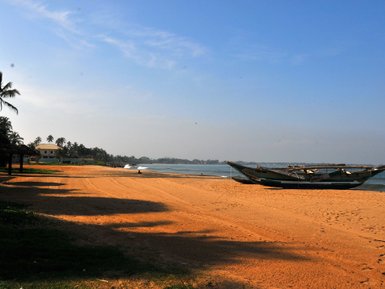 Kleines Boot liegt am orangenen Sandstrand vor tropischer Kulisse – Sri Lanka Familienreise