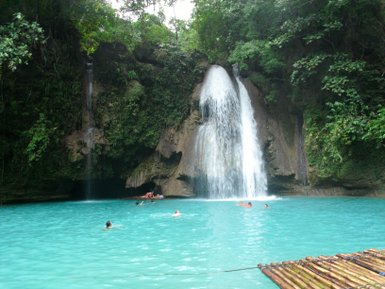 Ein atemberaubender Wasserfall stürzt in ein türkisfarbenes Becken, umgeben von üppigem Grün und fröhlichen Schwimmern.