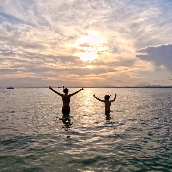 Zwei Personen stehen im Wasser und genießen den Sonnenuntergang, während sie fröhlich die Arme heben.