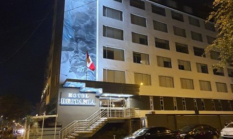 Das Hotel Britania in Miraflores, Peru, erstrahlt nachts mit einer beleuchteten Fassade und einer peruanischen Flagge.
