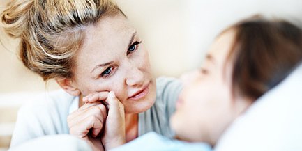 Eine besorgte Mutter schaut liebevoll auf ihr krankes Kind, das im Bett liegt und schläft.