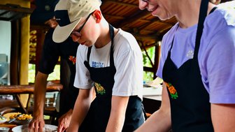 Drei Personen in Kochschürzen arbeiten voll konzentriert am Tisch mit Teig, während sie entspannt miteinander kommunizieren.