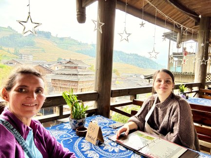 Zwei Frauen sitzen an einem Tisch in einem Restaurant mit Blick auf die terrassierten Reisfelder im Hintergrund.