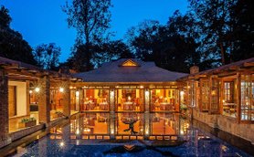 Ein elegantes Lodge-Gebäude mit großen Fenstern spiegelt sich im ruhigen Pool bei Dämmerungslicht wider.