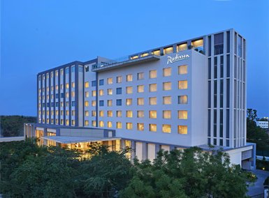 Das Radisson Hotel in Agra strahlt in der Dämmerung mit beleuchteten Fenstern und modernem Design, umgeben von Bäumen.