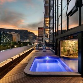 Ein eleganter Balkon mit einem kleinen Pool, umgeben von modernen Gebäuden und einer atemberaubenden Abendkulisse.