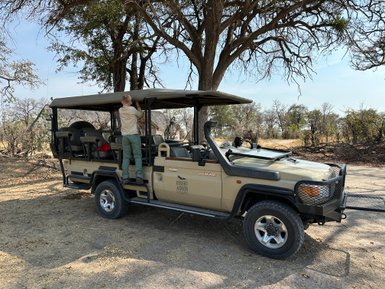 Ein Junge steht auf einem Geländewagen und schaut in die Umgebung, umgeben von Bäumen und trockenem Gras.