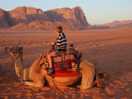 Kind sitzt beim Sonnenuntergang auf einem Kamel - Jordanien mit Kindern