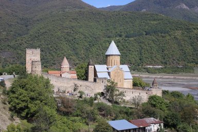 Eine beeindruckende Festung mit mehreren Türmen und einer Kirche, umgeben von üppigen grünen Bergen und einem klaren blauen Himmel.