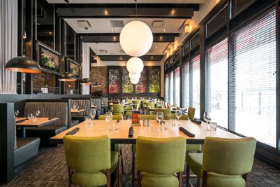Ein modernes Restaurant mit grünen Stühlen und eleganten Tischen, beleuchtet von großen, runden Lampen.