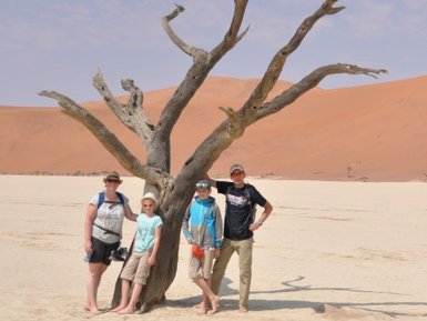 Eine Familie steht neben einem trockenen Baum in der Wüste - Namibia Rundreise mit Kindern