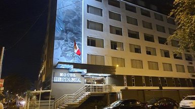 Das Hotel Britania in Miraflores, Peru, erstrahlt nachts mit einer beleuchteten Fassade und einer peruanischen Flagge.