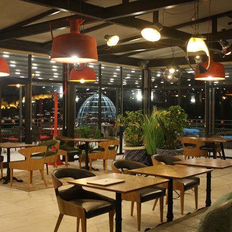 Ein stilvolles Restaurant mit modernen Möbeln, großen Fenstern und einer beeindruckenden Aussicht auf die Stadt bei Nacht.