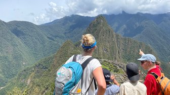 Eine Gruppe von Menschen steht auf einem Aussichtspunkt und bewundert die Ruinen von Machu Picchu inmitten der Berge.