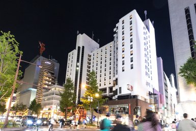 Ein modernes Hotelgebäude mit beleuchteten Fenstern, umgeben von urbaner Architektur und nächtlicher Atmosphäre.