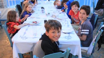 Eine Gruppe von Kindern sitzt fröhlich an einem Tisch, umgeben von einer schönen Aussicht auf das Wasser.