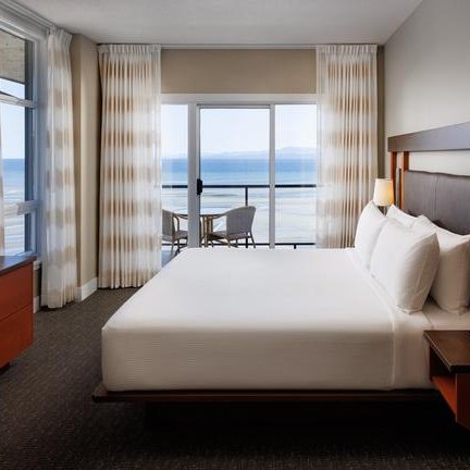 Ein modernes Hotelzimmer mit einem großen Bett, einem Fernseher und einem Balkon mit Blick auf das Meer.